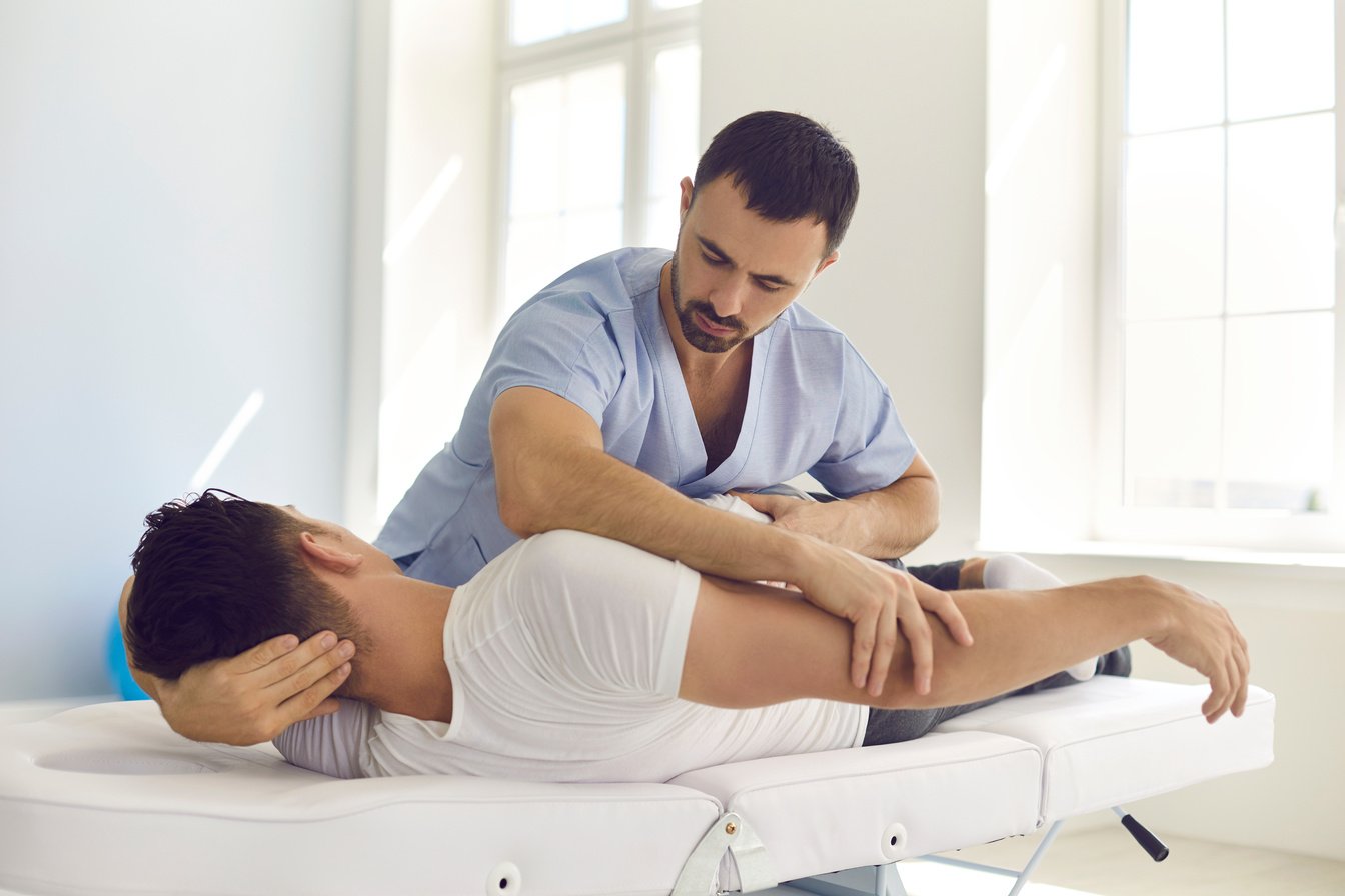 Chiropractor, Osteopath, Physiotherapist or Manual Therapist Working with Young Man in Modern Clinic